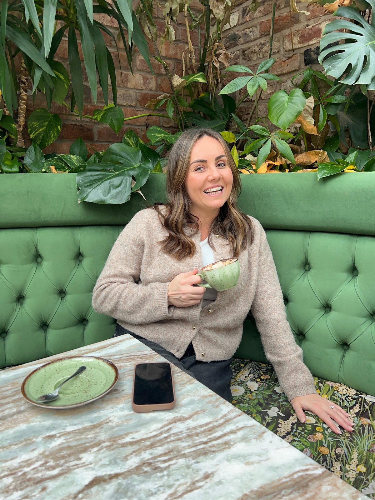 Leigh-Anne, founder of The Sisterhood, laughing with a coffee on a green sofa