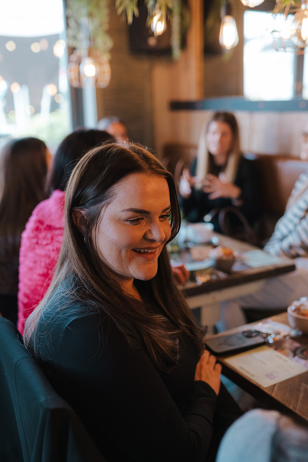 A woman smiling at a catch-up table with others chatting behind her
