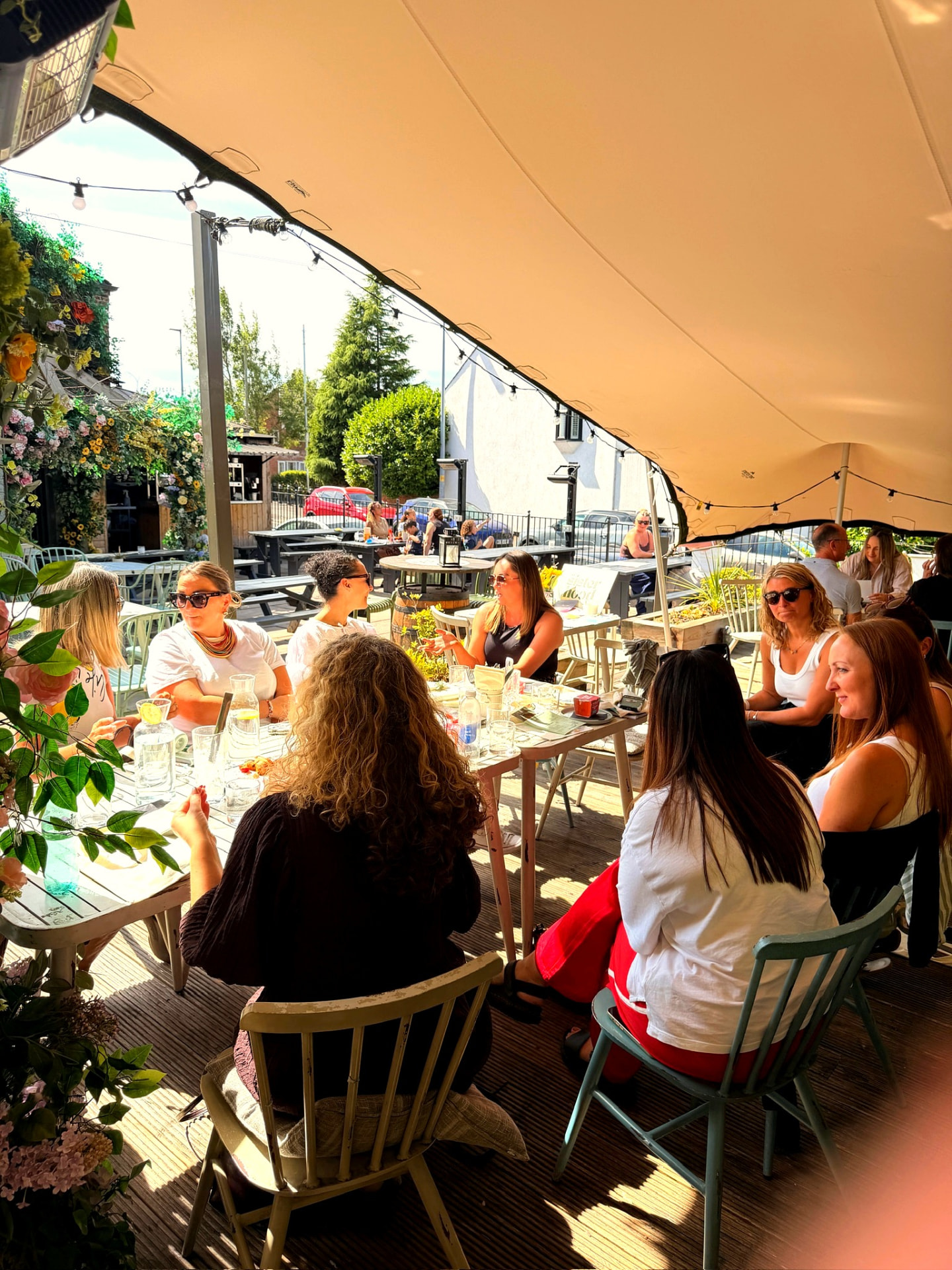 A sunny outdoor catch-up under a canopy, women chatting round long tables