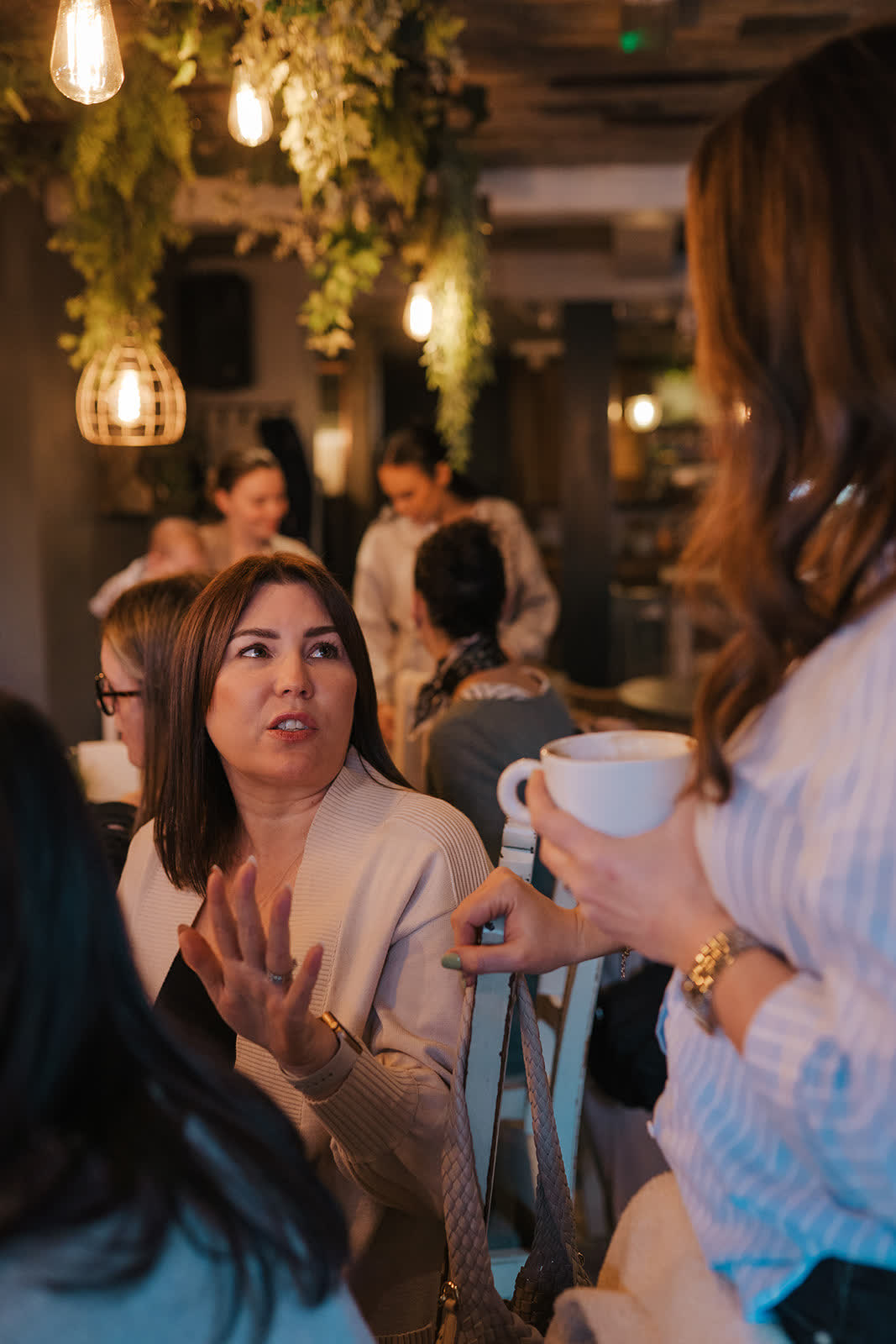 A busy cafe room of women chatting, one holding a cappuccino