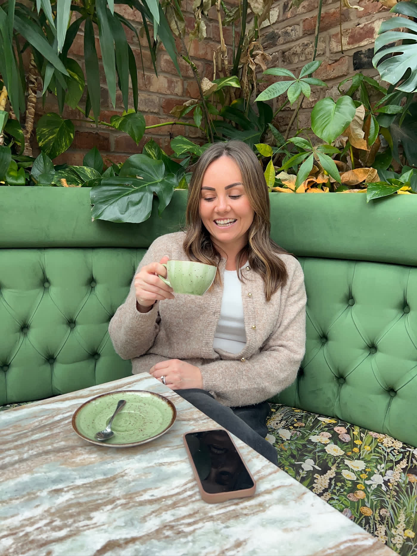 Leigh-Anne, founder of The Sisterhood, laughing over a coffee on a green velvet banquette